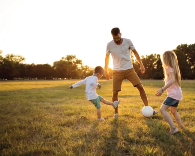 Father playing soccer outdoors with boy and girl children
