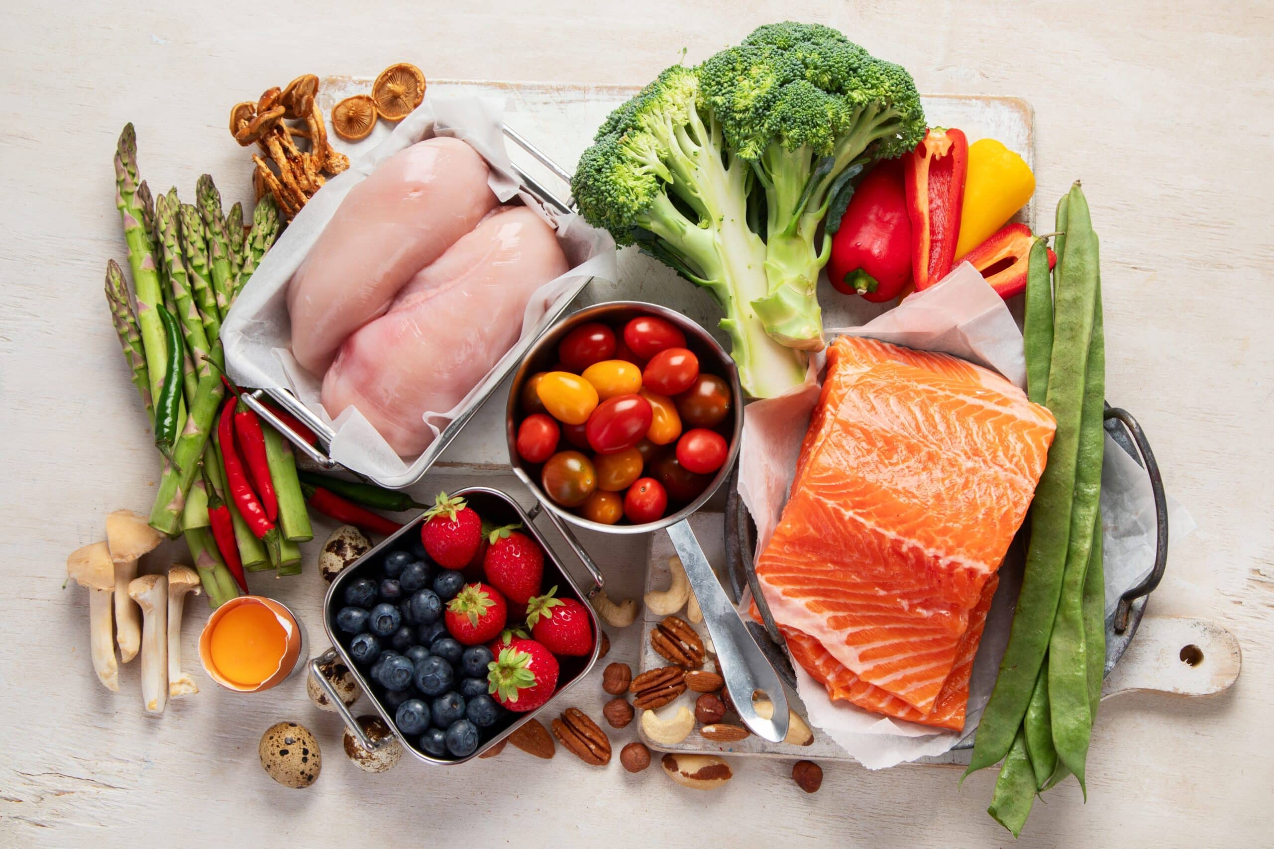 Various healthy heart food; vegetables, nuts, and proteins laid out on off-white background